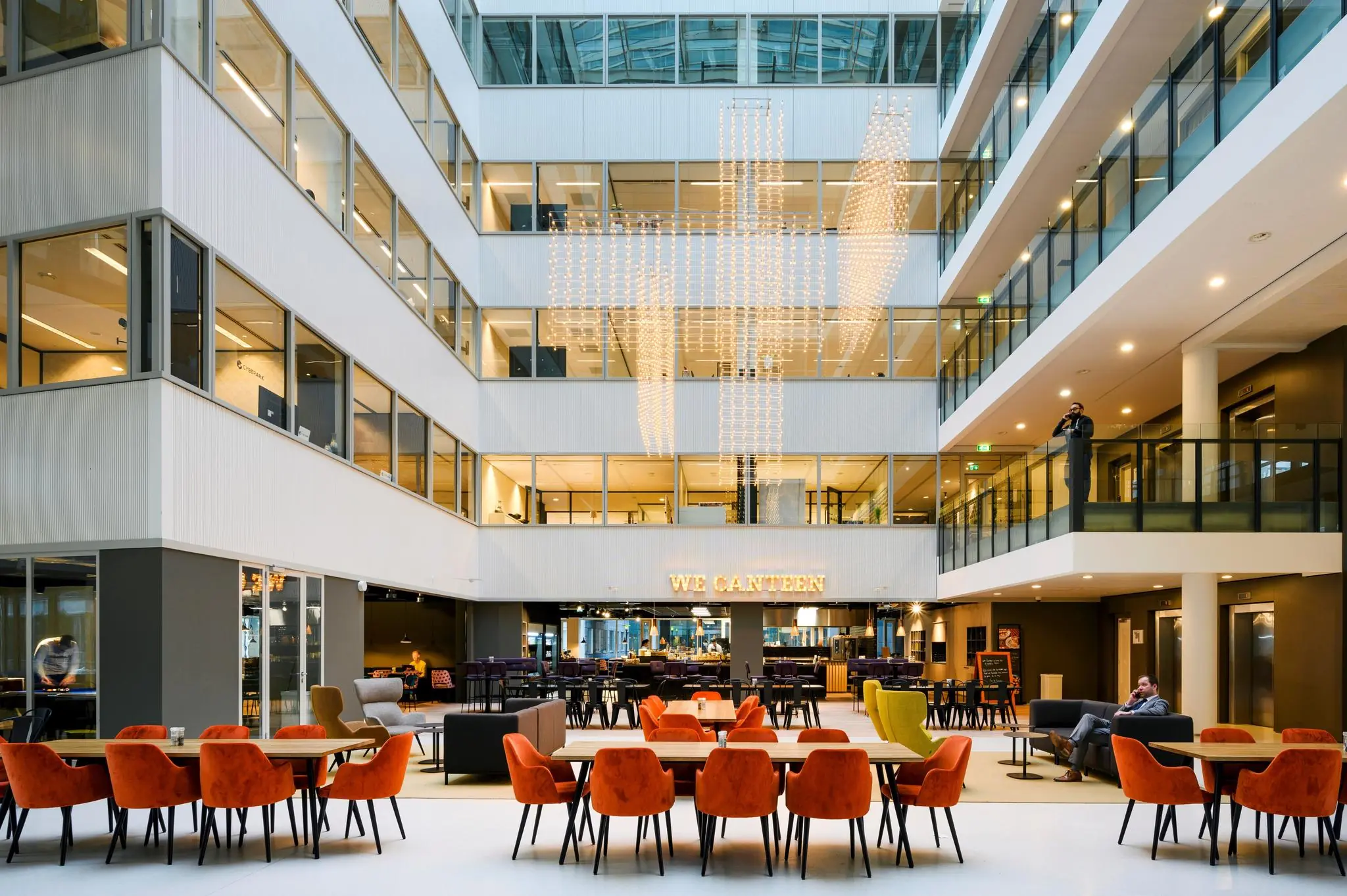 Modern bedrijfsrestaurant met feloranje stoelen in een open atrium aan de Thomas R. Malthusstraat.